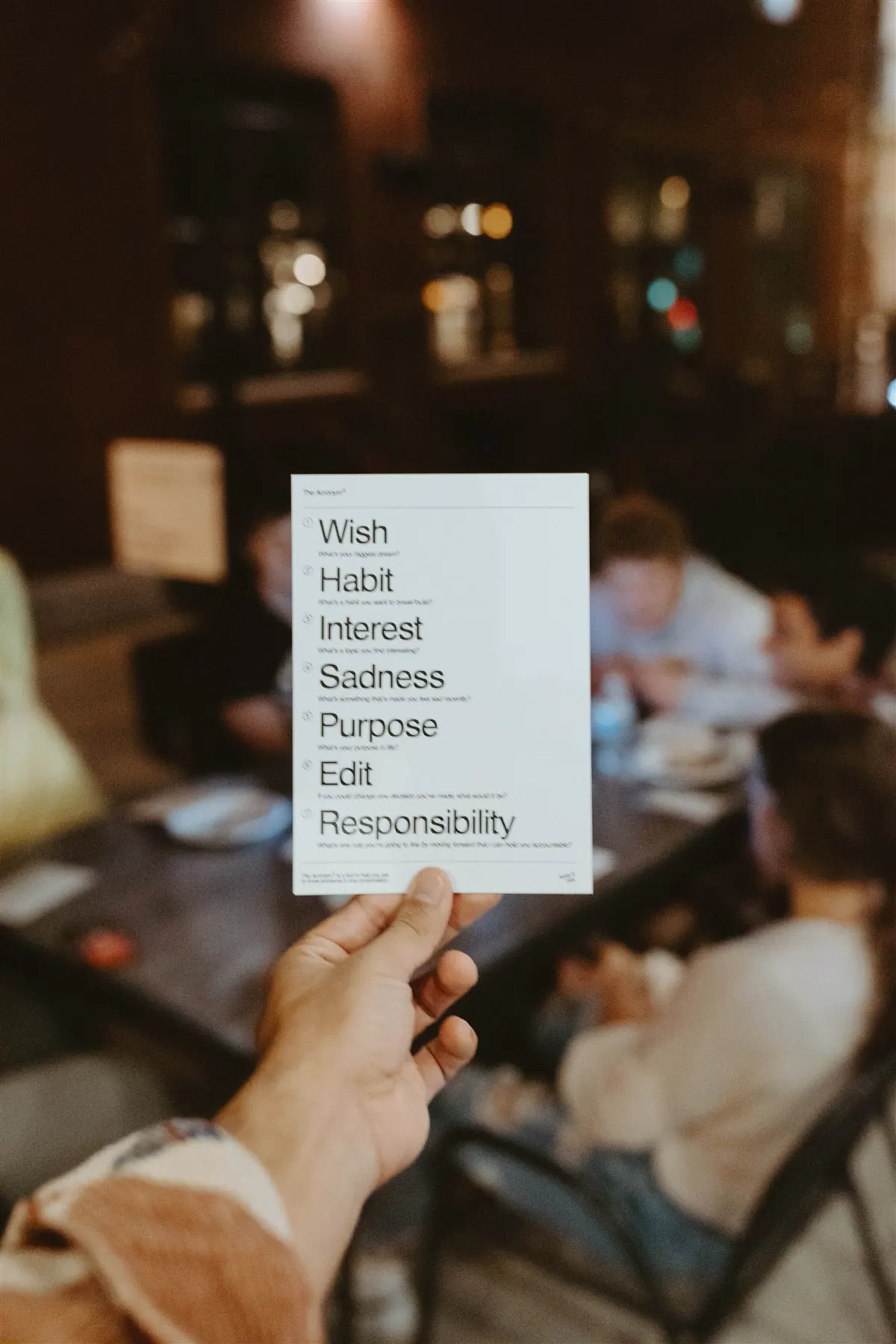 A hand holding an icebreaker card listing Wish, Habit, Interest, Sadness and Purpose