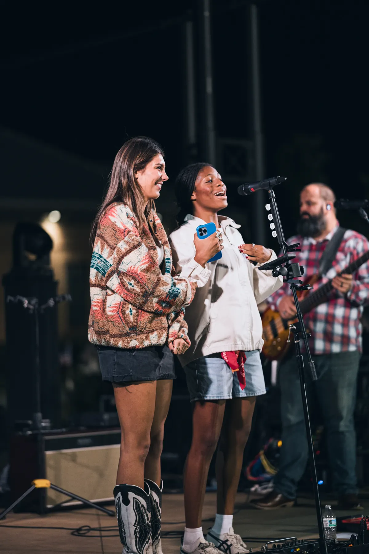 Two students laughing together on stage at an evening Whisper event